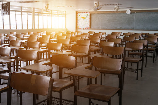 Filas de pupitres en un aula con una pizarra al fondo