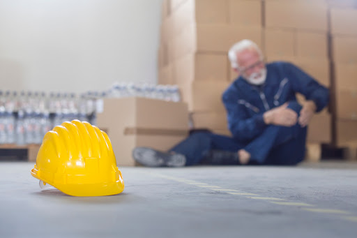 Un trabajador sentado en el suelo sujetándose la rodilla tras una lesión laboral