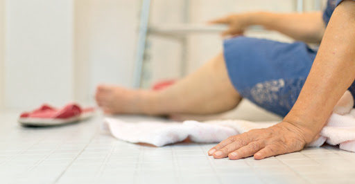 An elderly woman sits on the bathroom floor after a slip and fall accident