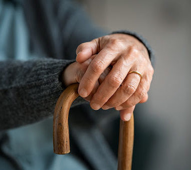 An elderly person holding onto a curved wooden cane