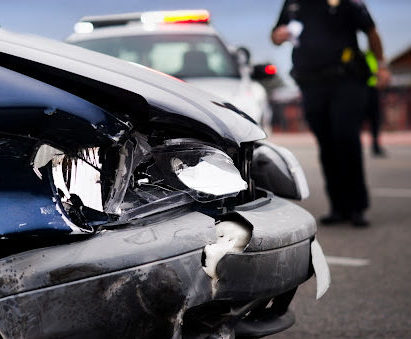 A police officer approaching the front end of a damaged car after an accident