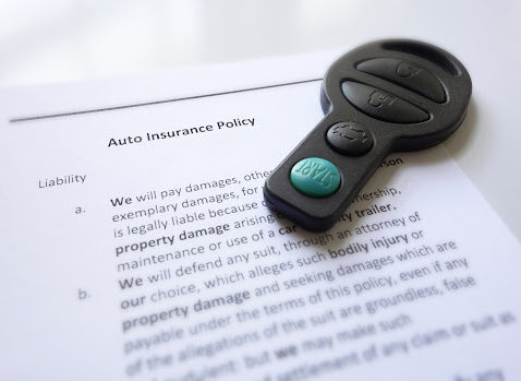 A remote car key sitting on top of a car insurance policy