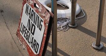 No lifeguard sign near pool with life preserver in the background.