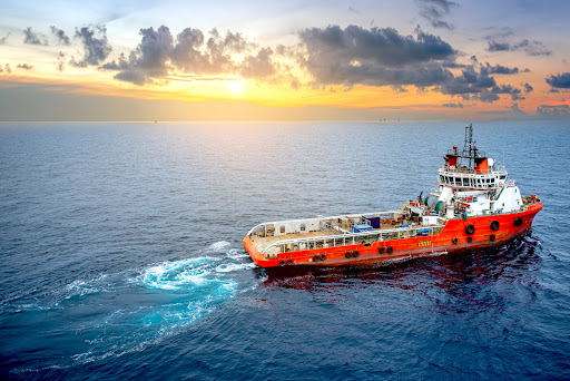 An orange maritime vessel traveling the water in front of a sunset