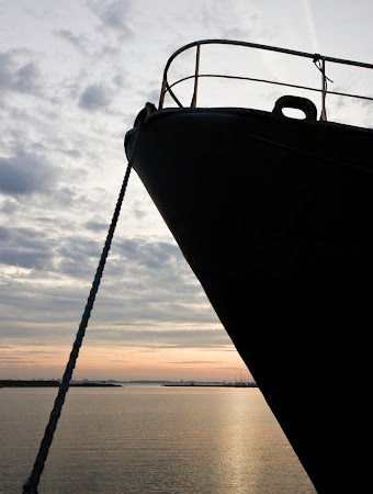 The silhouette of the bow of a large ship and a rope tying it to a dock at dawn