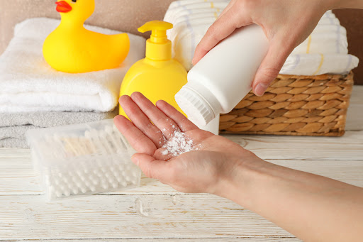 A person shaking talcum powder into their hand in front of a bathroom counter