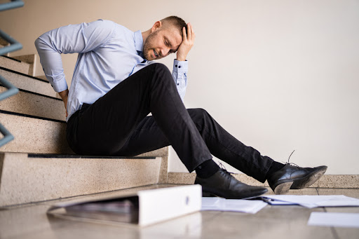 A young man at work holding his head after falling on some stairs