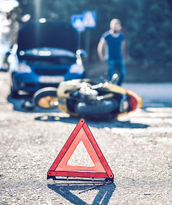 A warning triangle sitting on the pavement in front of a motorcycle accident