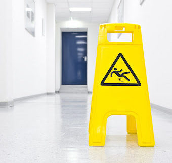 A wet floor sign sitting in a bright white hallway with a blue door in the background