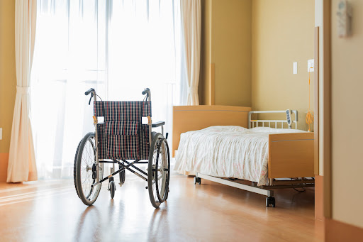 A wheelchair and small bed in a room at a nursing home in Gonzales