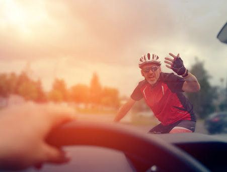 A bicyclist looks angry as seen from the drivers seat of a car