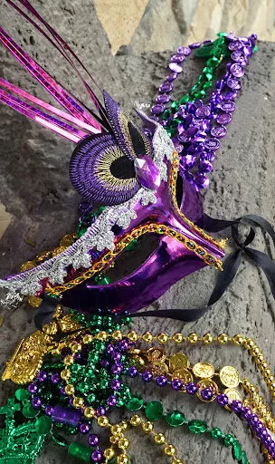 A mask and beads lying on a cement curb after a Mardi Gras parade