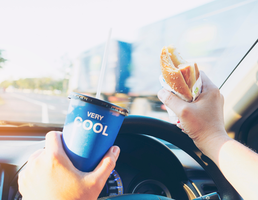 driver heading a sandwich and drinking soda while driving
