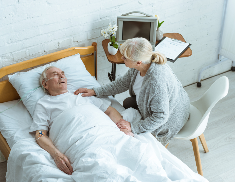 older man in coma with wife holding his side