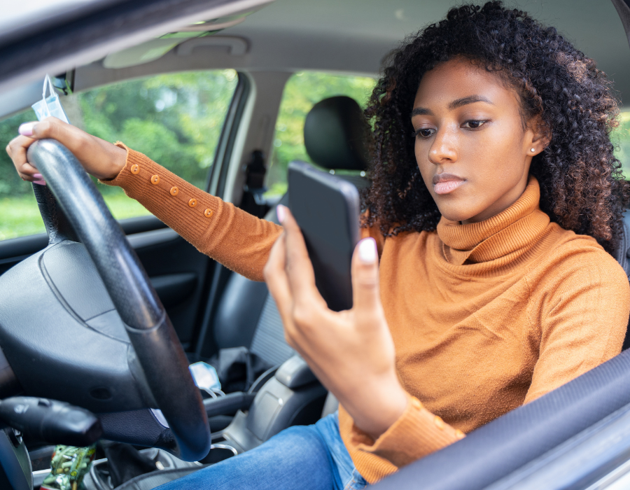 woman in orange sweater on her phone while driving