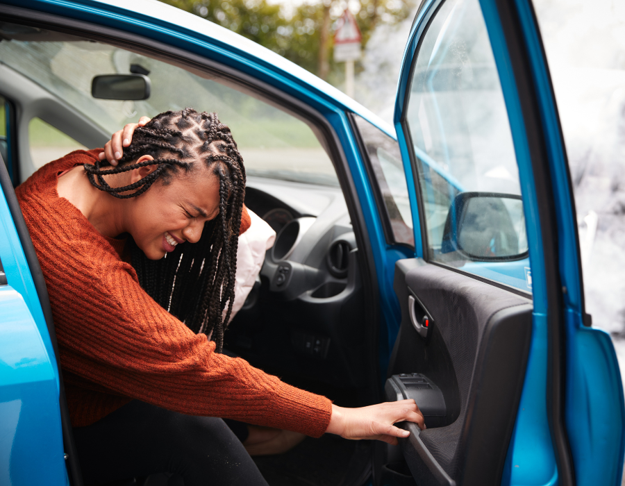 woman holding head to get out of car after accident