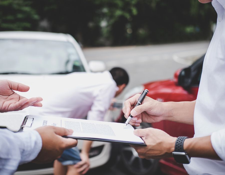 man signing paperwork infront of car accident