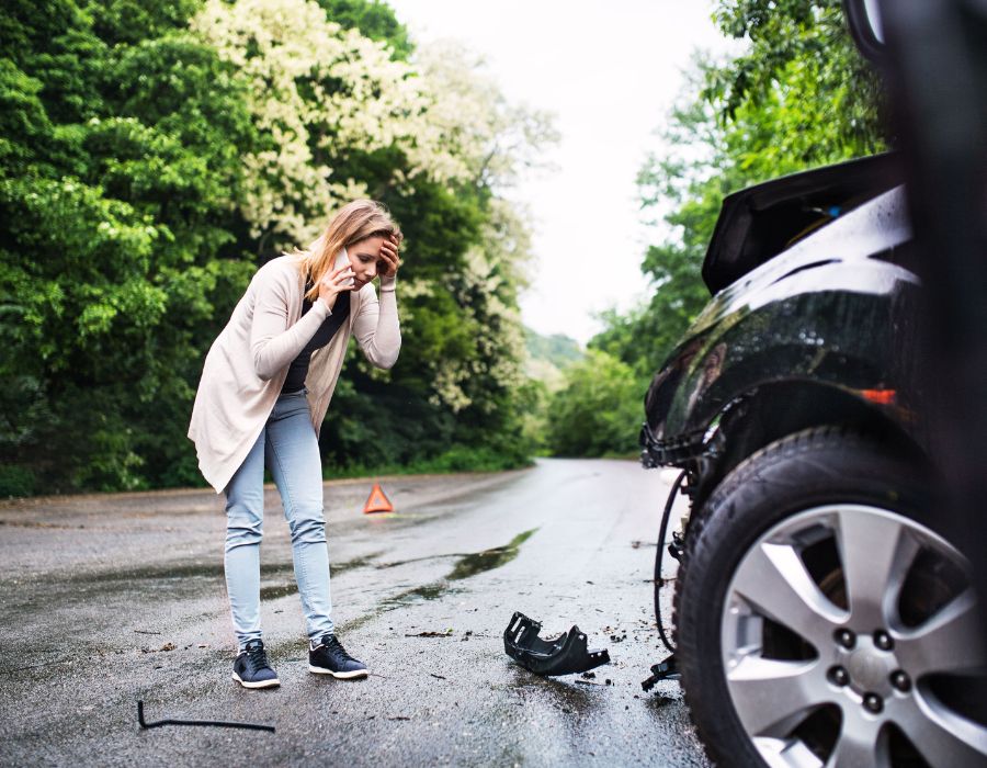 woman on phone after car accident with debris in the road