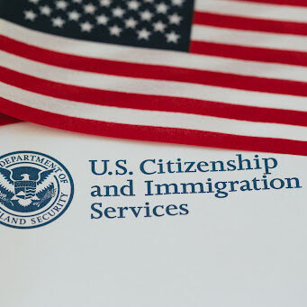 US flag and citizenship and immigration paperwork Immigration Lawyer, U.S. Citizenship and Immigration Services pamphlet