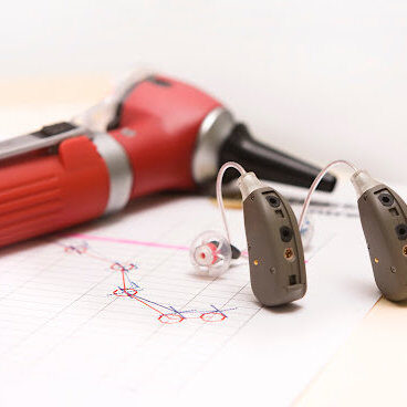 Hearing-Aids-and-Otoscope A pair of modern hearing aids on a medical chart showing a hearing loss of high frequencies. An otoscope lies in the background.