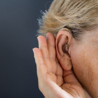 Woman with Hearing Aid Elderly woman with hearing aid on grey background. Deafness and hearing loss concept.