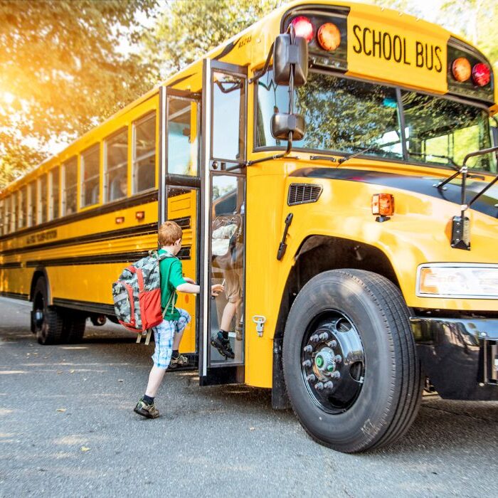 school bus image Little kid in green jacket with red backpack getting on school bus
